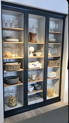 an open cabinet with glass doors and shelves filled with plates, bowls and other items