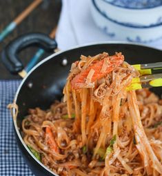 the noodles are being lifted from the pan by tongs