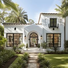 a white house with lots of windows and plants on the front lawn, surrounded by palm trees