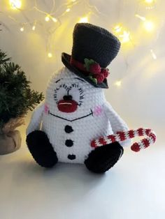 a crocheted snowman sitting next to a christmas tree