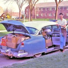 a man standing next to an old car with boxes on the hood and open trunk