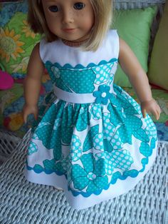 a doll is sitting on a bed wearing a blue and white dress with polka dots