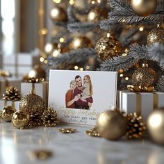 a christmas card sitting on top of a table next to gold ornaments and presents under a christmas tree