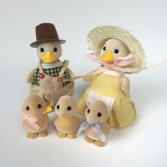 three stuffed animals are posed next to each other on a white surface, one is wearing a hat and the other has a yellow dress