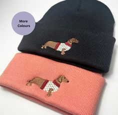 two knitted hats with embroidered dogs on them, one is pink and the other is black