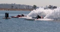 two speed boats are spraying water on the lake while another boat is in the background