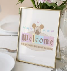 a welcome sign on a table with flowers in a vase next to plates and utensils