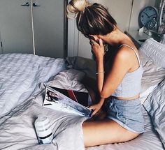 a woman sitting on top of a bed reading a magazine