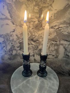 two white candles sitting on top of a marble plate next to a wallpapered background