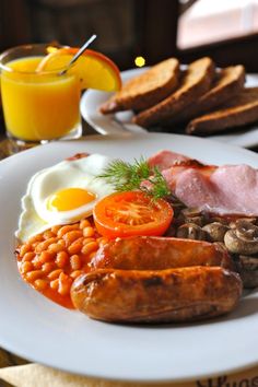 a white plate topped with eggs, sausages and beans next to toasted bread