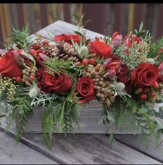 a wooden box filled with lots of red flowers and greenery on top of a table