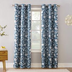 a blue and white floral curtain hanging in front of a window next to a wooden table