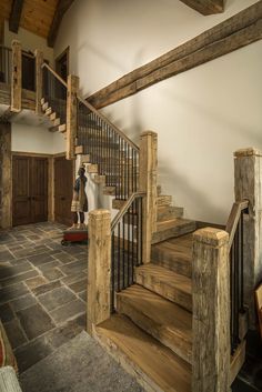 a wooden stair case in the middle of a room with stone floors and wood handrails