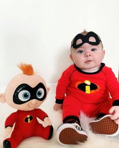 a baby sitting next to a stuffed toy wearing a red shirt and black eye mask