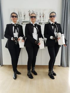 three women in black tuxedos are holding white bags and posing for the camera