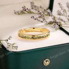 a gold wedding ring sitting on top of a green box next to some purple flowers