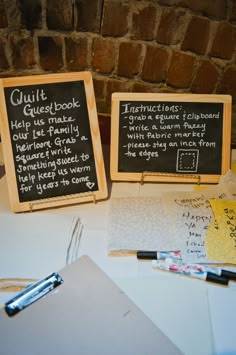 two blackboards with writing on them sitting on a table next to a brick wall