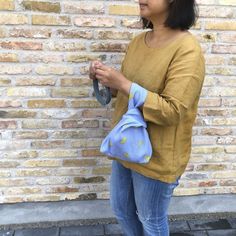 a woman standing in front of a brick wall holding a blue purse and looking at her cell phone