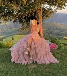 a woman in a pink dress sitting under a tree reading a book with her legs crossed