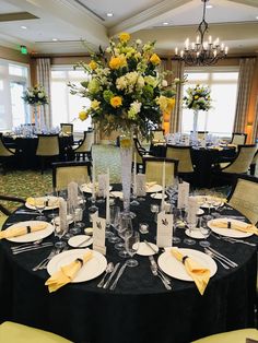 a dining room with black table cloths and yellow napkins on the place settings