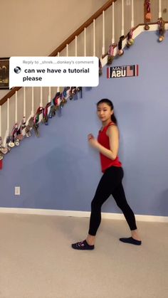 a woman in red shirt and black leggings standing next to stairs with an american flag on the wall