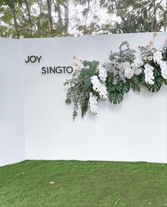 white flowers and greenery are arranged on the wall in front of joy singo