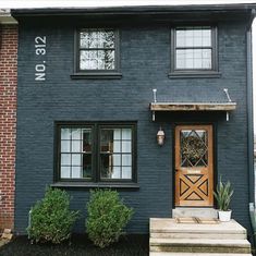 a black house with a wooden door and steps leading up to the front porch area