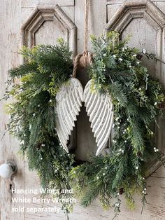 an angel wreath hanging on the front door with greenery and white berries around it