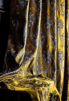 a yellow chair sitting next to a window covered in curtained fabric with an intricate design