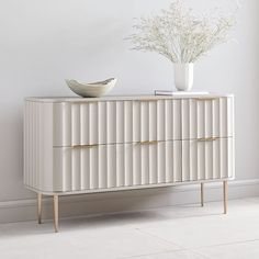 a white cabinet with two drawers and a bowl on top, in front of a wall