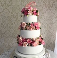 a three tiered cake with pink and white flowers on the top, sitting on a table