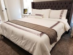 a large bed with white sheets and brown pillows in a bedroom next to a window