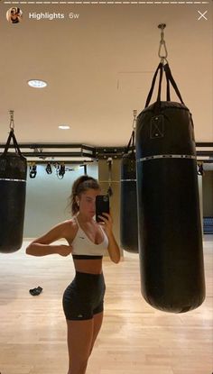 a woman is taking a selfie in front of a punching bag with her cell phone