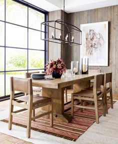 a dining room table with chairs and vases on it in front of a large window