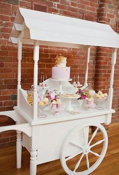 a white cart filled with lots of food on top of a hard wood floor next to a brick wall