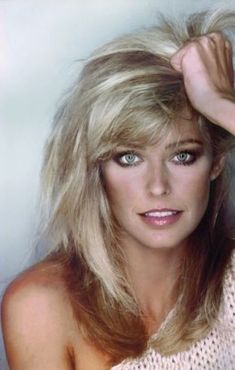 a woman with long blonde hair and blue eyes posing for a photo in front of a white background