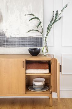 a wooden cabinet with plates and bowls on it in front of a wall mounted painting