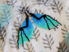 two pairs of beaded earrings with blue and green feathers hanging from it's hooks