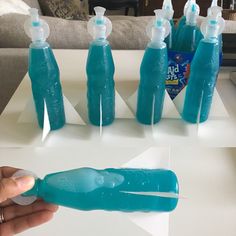 a hand holding a plastic bottle with several empty bottles in front of it on top of a table