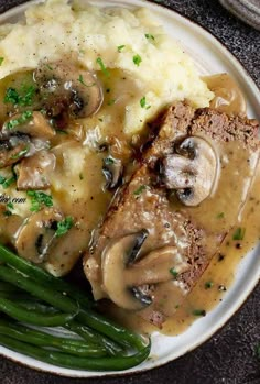 a white plate topped with meat covered in mushroom gravy and green beans