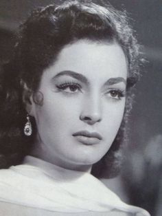 an old black and white photo of a woman with large earrings on her head, looking at the camera