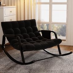 a black rocking chair sitting on top of a rug in front of a large window