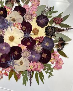 a bunch of flowers that are on top of a white tablecloth with green leaves