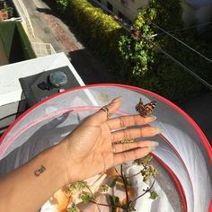 a woman's hand with two butterflies on her finger, in front of a house