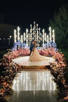 a bride and groom standing in front of a flower garden with lights on the side