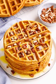 a stack of waffles sitting on top of a white plate next to a bowl of nuts