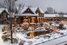 a large house covered in snow next to a tree and pond with lights on it