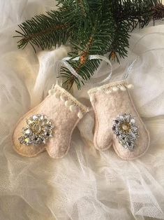 two baby's mittens hanging from a christmas tree with white fabric and pine needles