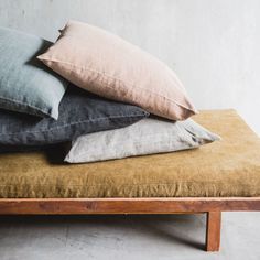 four pillows stacked on top of each other on a wooden bench in front of a white wall