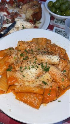 pasta with sauce and parmesan cheese on a white plate next to olives